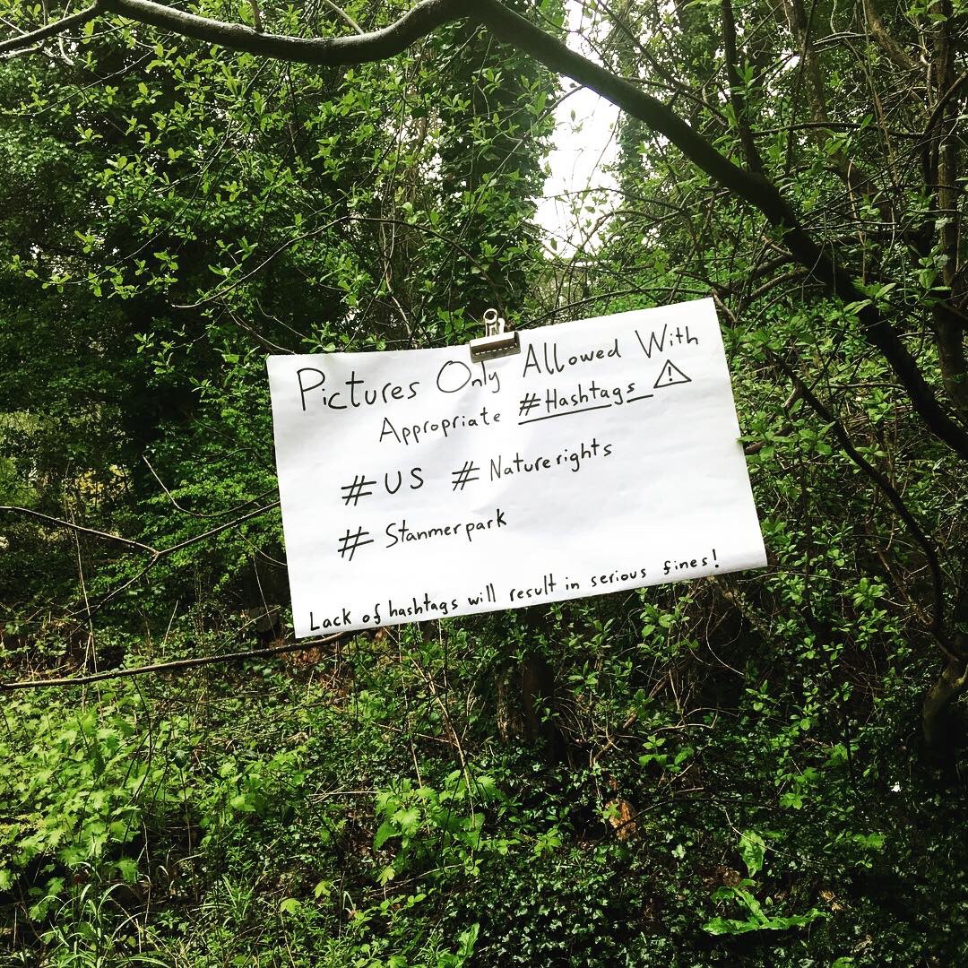 A note clipped to a tree in the woods reads 'Pictures only allowed with appropriate hashtags'.