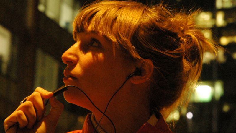 A woman in the city at night is about to record a message on a headset